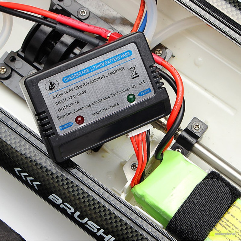 Cargador y cableado de la Lancha RC Fei Lun FT011 65cm con pack de batería LiPo, conexiones rojas y negras, carcasa negra y detalles en fibra de carbono