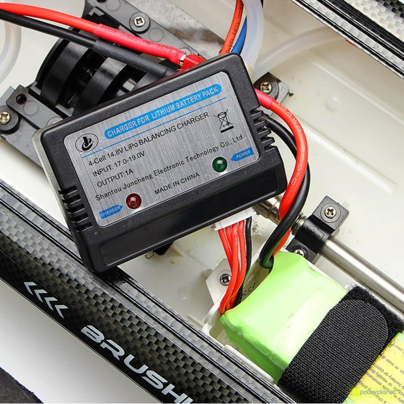 Cargador y cableado de la Lancha RC Fei Lun FT011 65cm con pack de batería LiPo, conexiones rojas y negras, carcasa negra y detalles en fibra de carbono