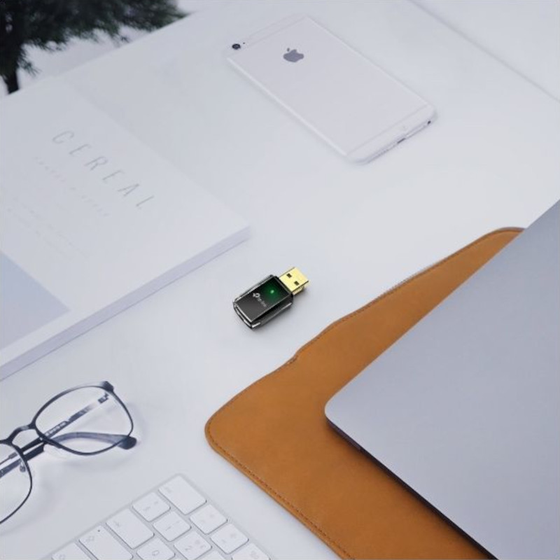 TP-Link Archer T2U Adaptador USB Wi-Fi 5 AC600 compacto negro con conector dorado, tapa transparente y LED verde, junto a portátil y teclado en escritorio