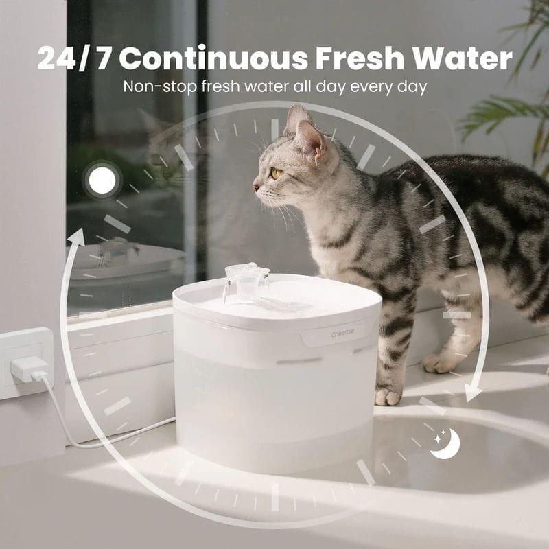 Bebedero automático blanco para gatos con depósito translúcido, flujo continuo de agua y boquilla elevada; diseño compacto junto a ventana y cable USB