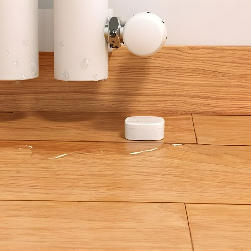 Sensor inteligente de fuga de água/inundação ZigBee SONOFF SNZB-05P +bateria em formato compacto branco no chão de madeira, detectando água sob