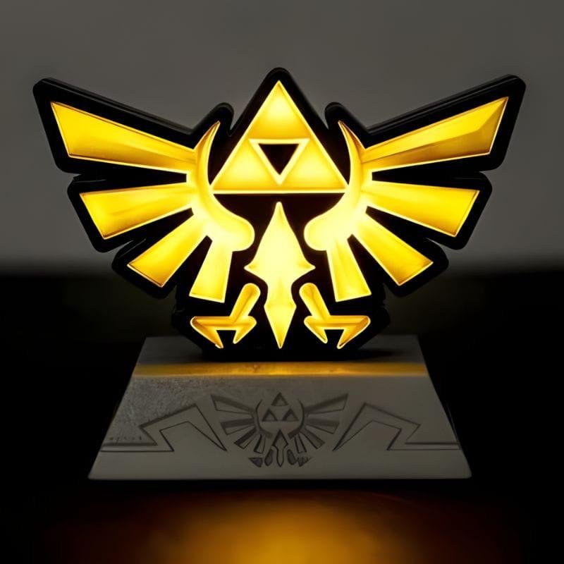 Lámpara Paladone Icon Hyrule Crest: emblema dorado de Trifuerza y águila, luz LED amarilla cálida, base gris con relieve, ideal para fans de Zelda.