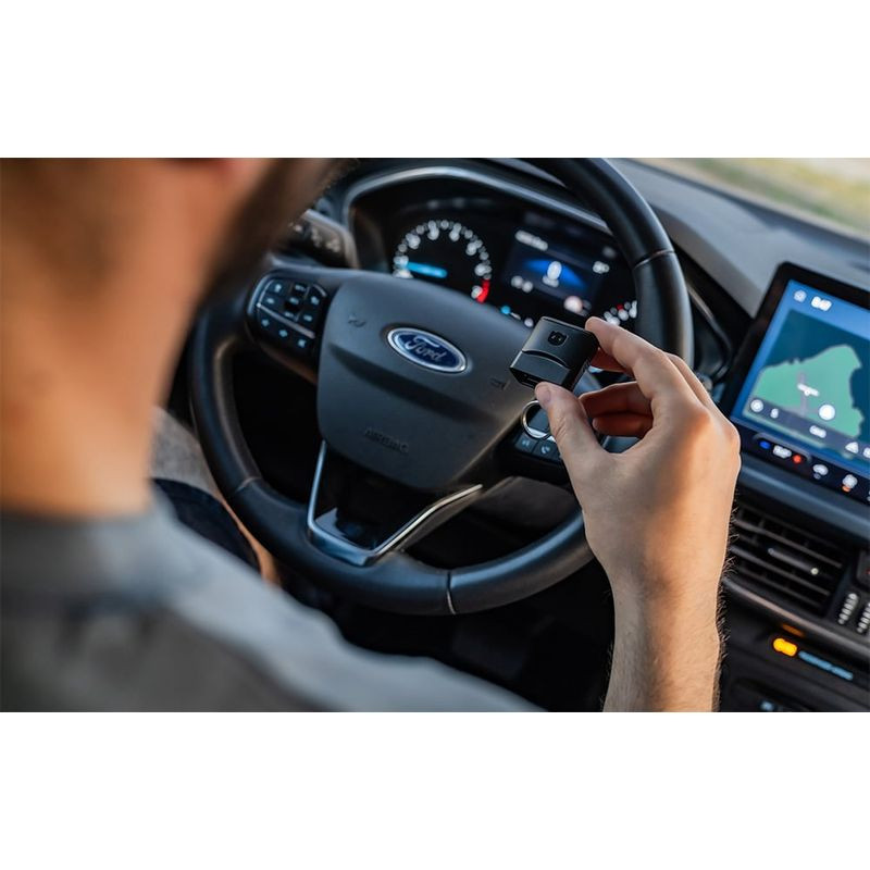 Scanner de diagnostic OBDeleven 3 compact tenu en main dans une voiture Ford, boîtier noir avec logo, conçu pour se brancher au port OBD et analyser le