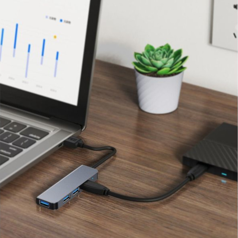 Hub USB BYL-2013U 4 en 1 gris, compacto de aluminio, con puertos USB 3.0 y USB 2.0, conectado a laptop y disco externo sobre escritorio de madera