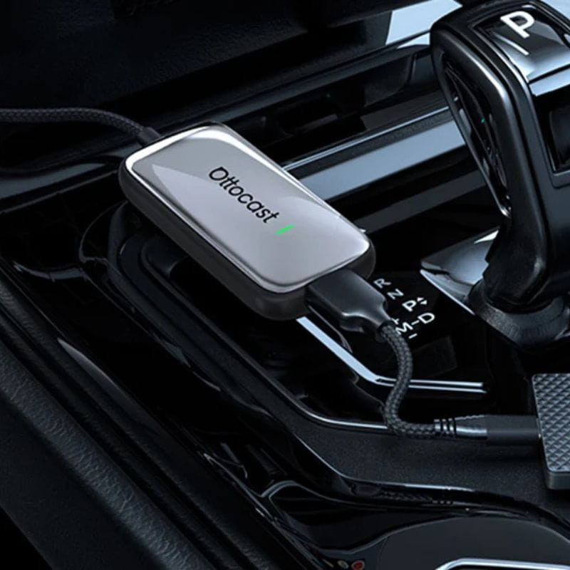 Ottocast Play2Video Ultra, adaptador compacto con carcasa metálica gris, logo iluminado y cable trenzado USB conectado en la consola del auto