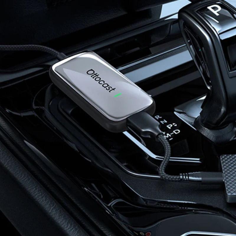 Ottocast Play2Video Ultra, adaptador compacto con carcasa metálica gris, logo iluminado y cable trenzado USB conectado en la consola del auto