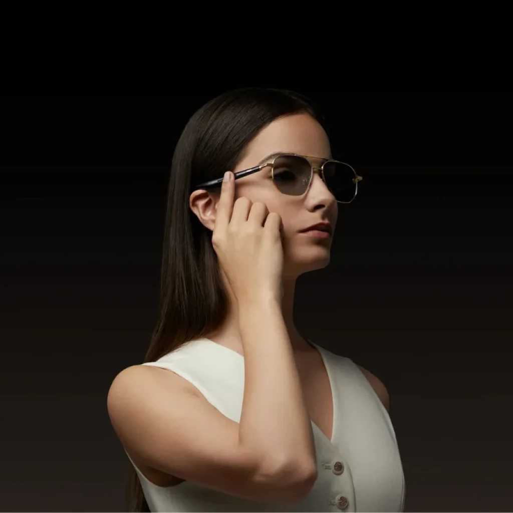 Gafas piloto con montura metálica dorada, lentes oscuras y patillas negras delgadas; diseño open ear para audio discreto y conectividad Bluetooth 5.4