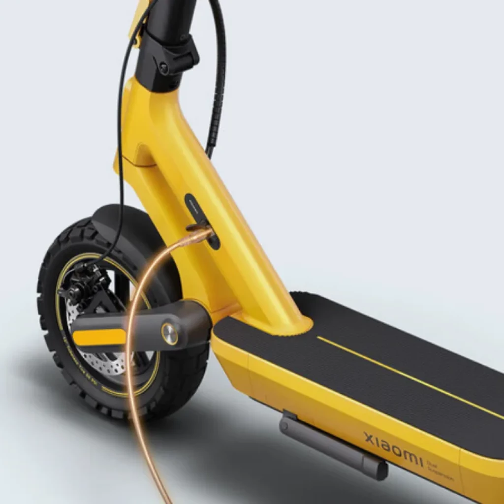 Carregador rápido 268W conectado a scooter elétrica amarela Xiaomi; cabo dourado, porta lateral no quadro, deck preto com faixa amarela e pneu robusto com