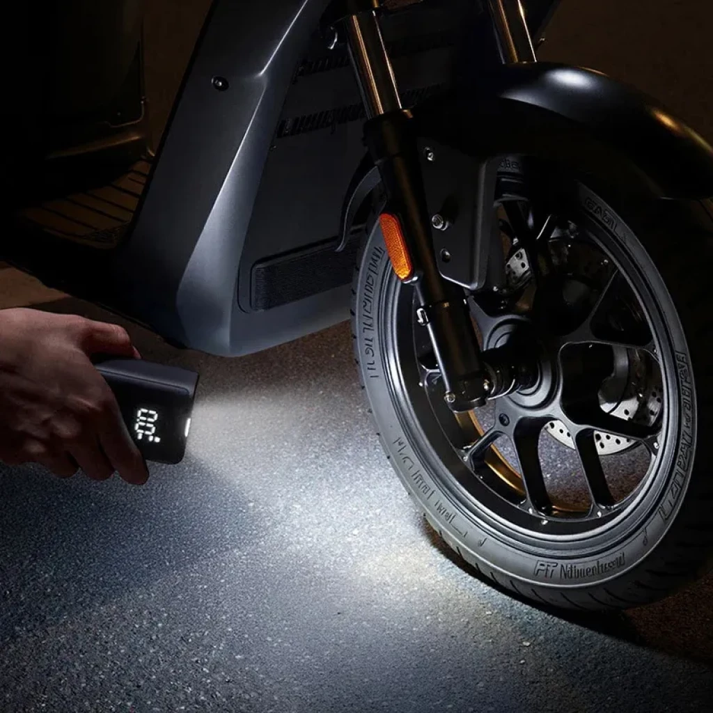 Mijia Compact Portable Electric Air Compressor con linterna ilumina y muestra pantalla digital mientras infla neumático de scooter