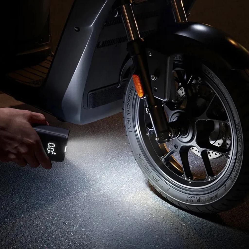 Mijia Compact Portable Electric Air Compressor con linterna ilumina y muestra pantalla digital mientras infla neumático de scooter