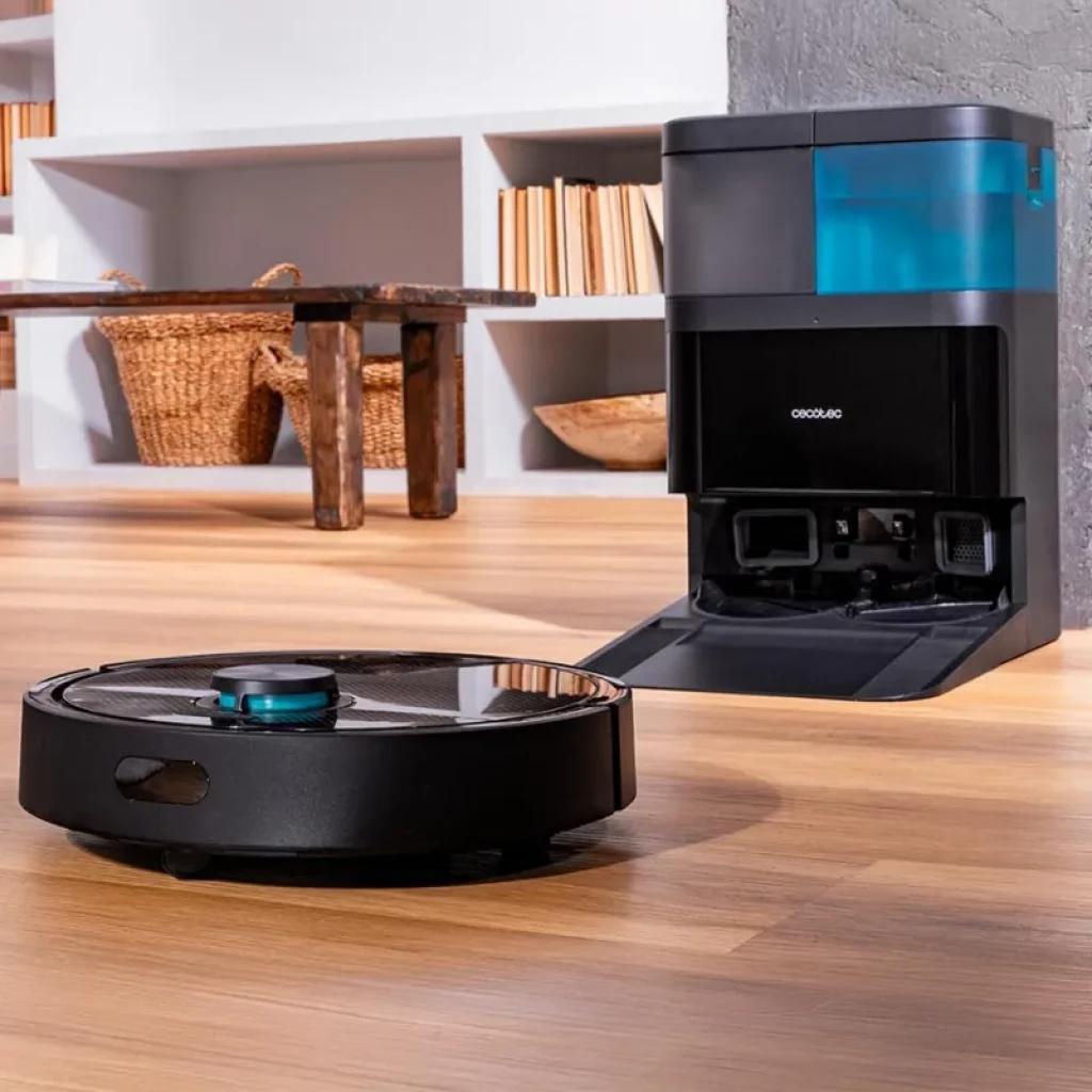 Cecotec Conga 15090 SpinArm robot negro con torreta láser y tapa metálica junto a base de autovaciado negra con depósito azul translúcido en suelo de madera