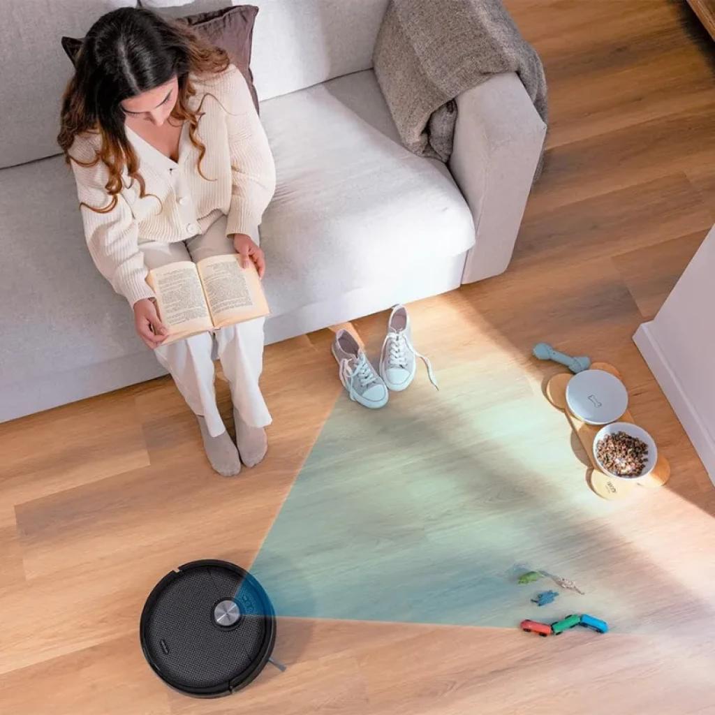 Cecotec Conga 15090 SpinArm robot negro con tapa plateada limpiando suelo de madera; mapea con luz azul y esquiva juguetes, comedero y obstáculos cerca