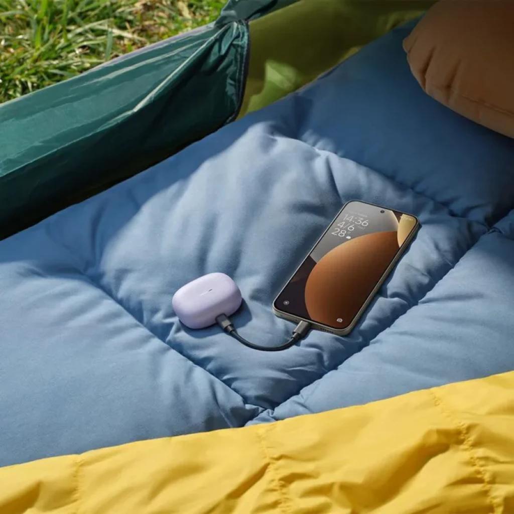 Xiaomi Redmi Note 15 Pro 5G preto sobre colchão azul, tela grande com bordas finas exibindo hora e clima, conectado por cabo a estojo lilás de earbuds