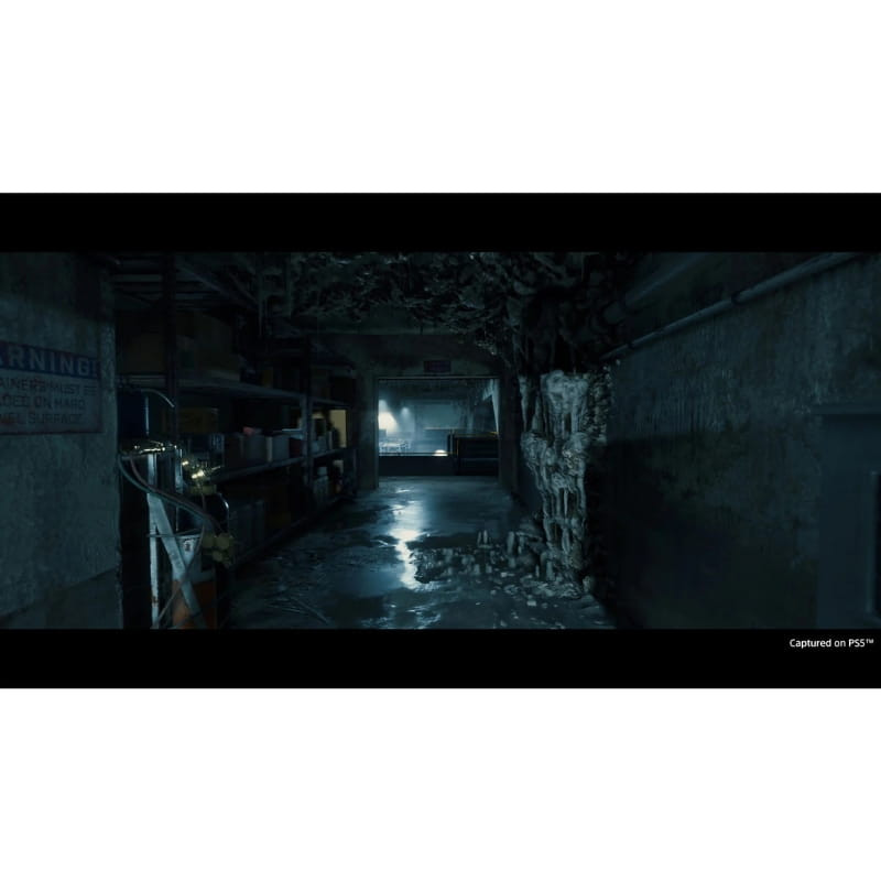 Couloir industriel sombre et humide, flaques au sol, murs délabrés et câbles, lumière froide au fond; ambiance post apocalyptique sur PS5 Director’s Cut