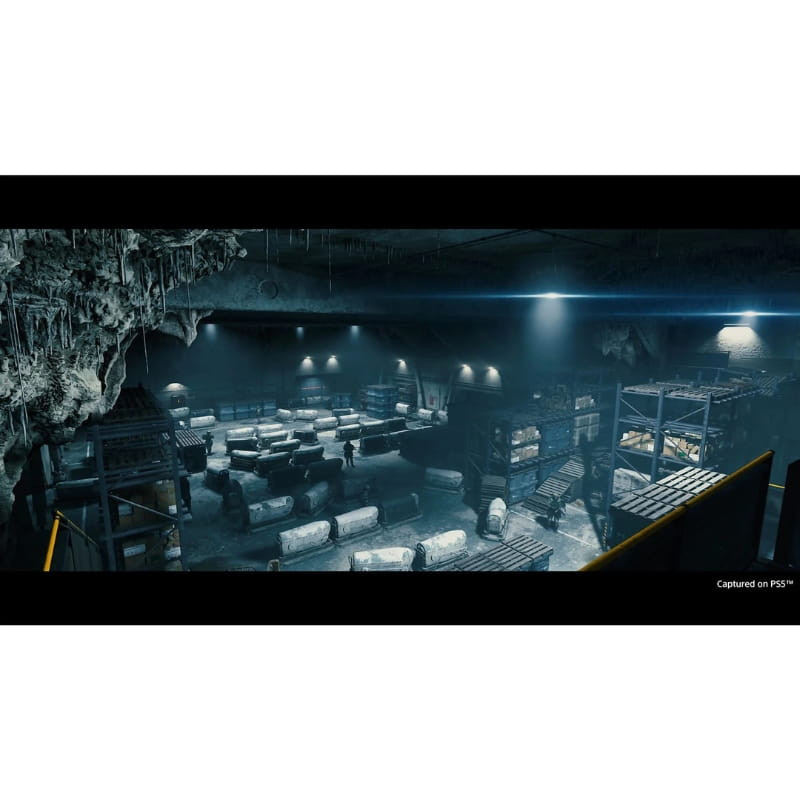 Capture PS5 de Death Stranding Directors Cut montrant un entrepôt souterrain sombre, étagères métalliques, colis cylindriques, stalactites et éclairage
