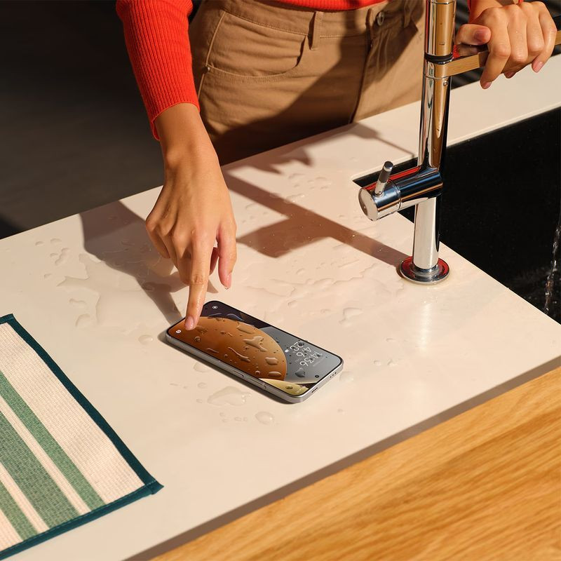 Xiaomi Redmi Note 15 Pro 5G 8Go/256Go Titane posé sur un plan de travail mouillé, écran allumé avec gouttes d’eau, design fin et élégant près d’un