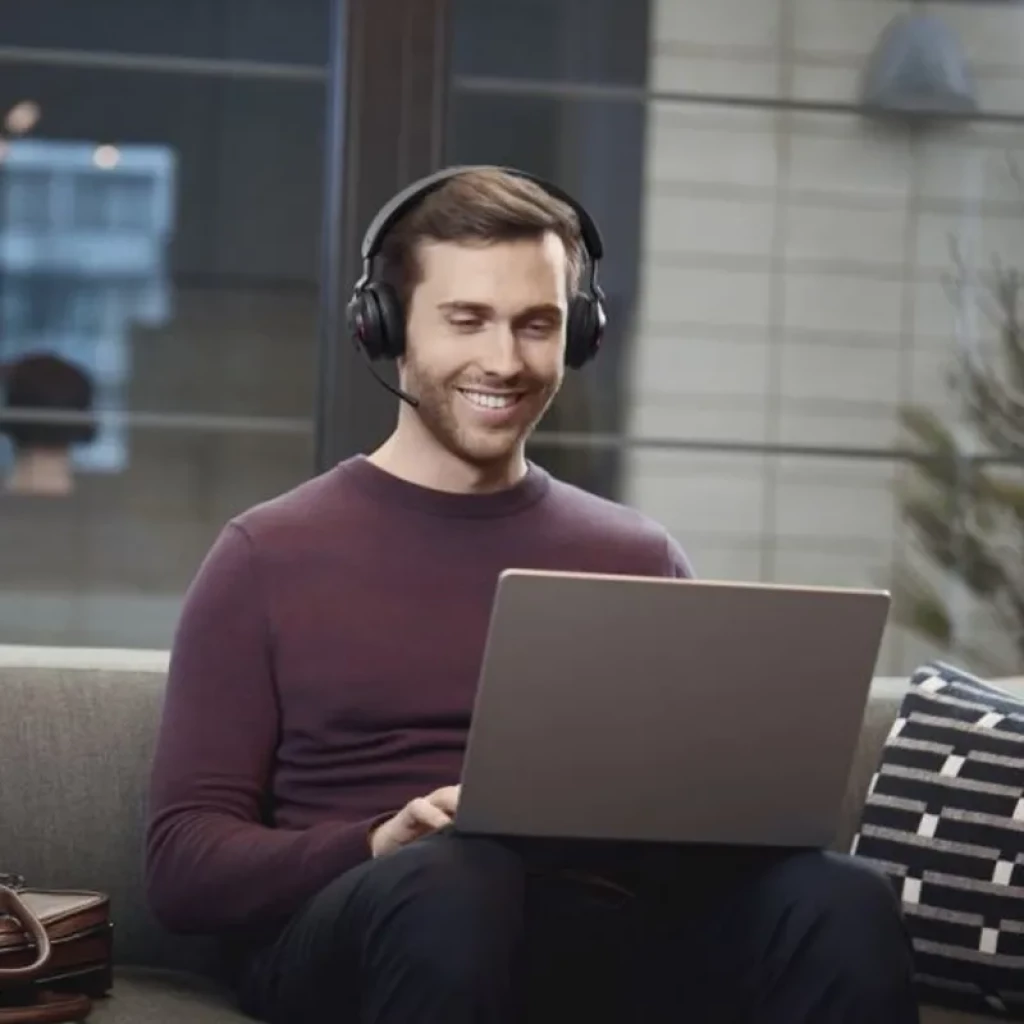 Hombre usando auriculares Jabra Evolve2 65 Stereo con micrófono abatible, diadema acolchada y cascos negros, trabajando en laptop en sala luminosa