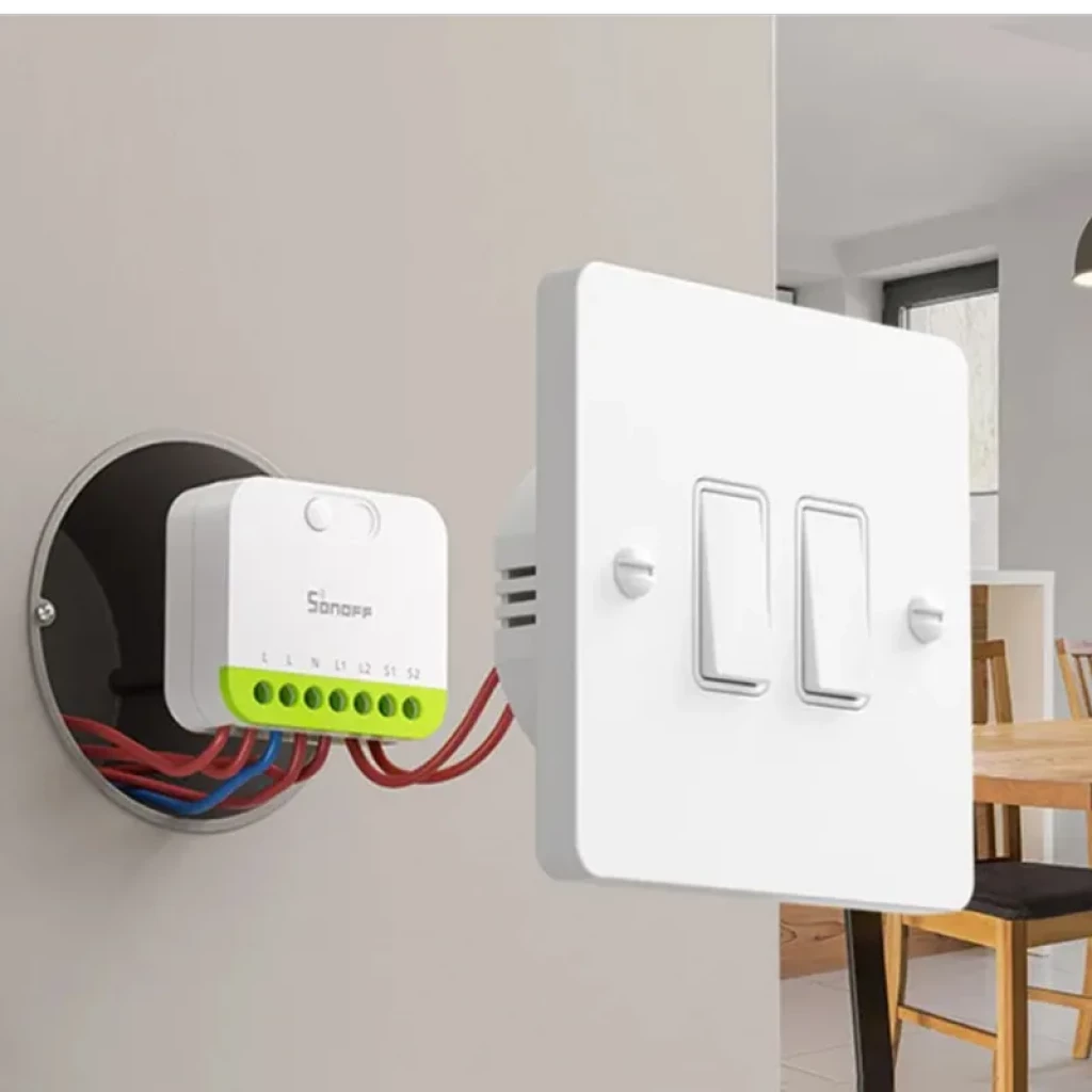 Sonoff MINI-ZB2GS ZigBee dos canales: módulo compacto con bornes verdes y cables, junto a placa blanca de doble interruptor, ideal para control domótico
