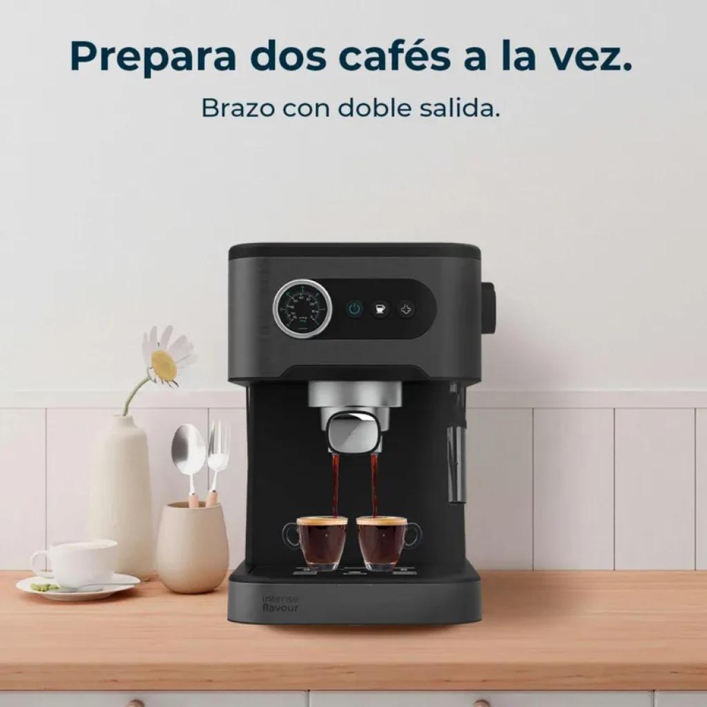 Cafetera express negra con manómetro circular, brazo con doble salida, dos tazas sirviéndose, depósito lateral transparente y botones frontales iluminados