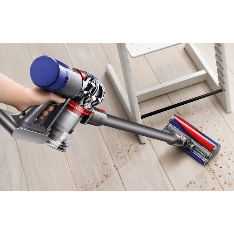 Dyson V8 Cyclone em ação: aspirador sem fios com cabeça motorizada rolo macio, limpa migalhas no chão de madeira; corpo cinza com detalhes vermelhos e azuis