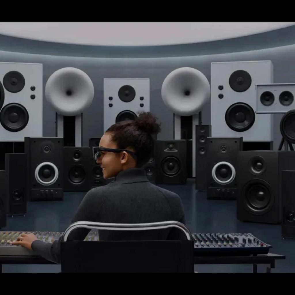 Jeune femme portant AR RayNeo Air 3S Pro eyepiece, lunettes AR noires, monture épaisse et verres fumés, testées en studio audio entouré d’enceintes