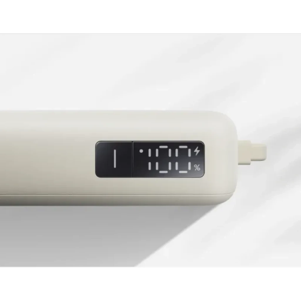 Banco de energía beige compacto con display numérico 100% y cable integrado lateral; acabado mate, puerto oculto y potencia 67W, 10000mAh visible en pantalla