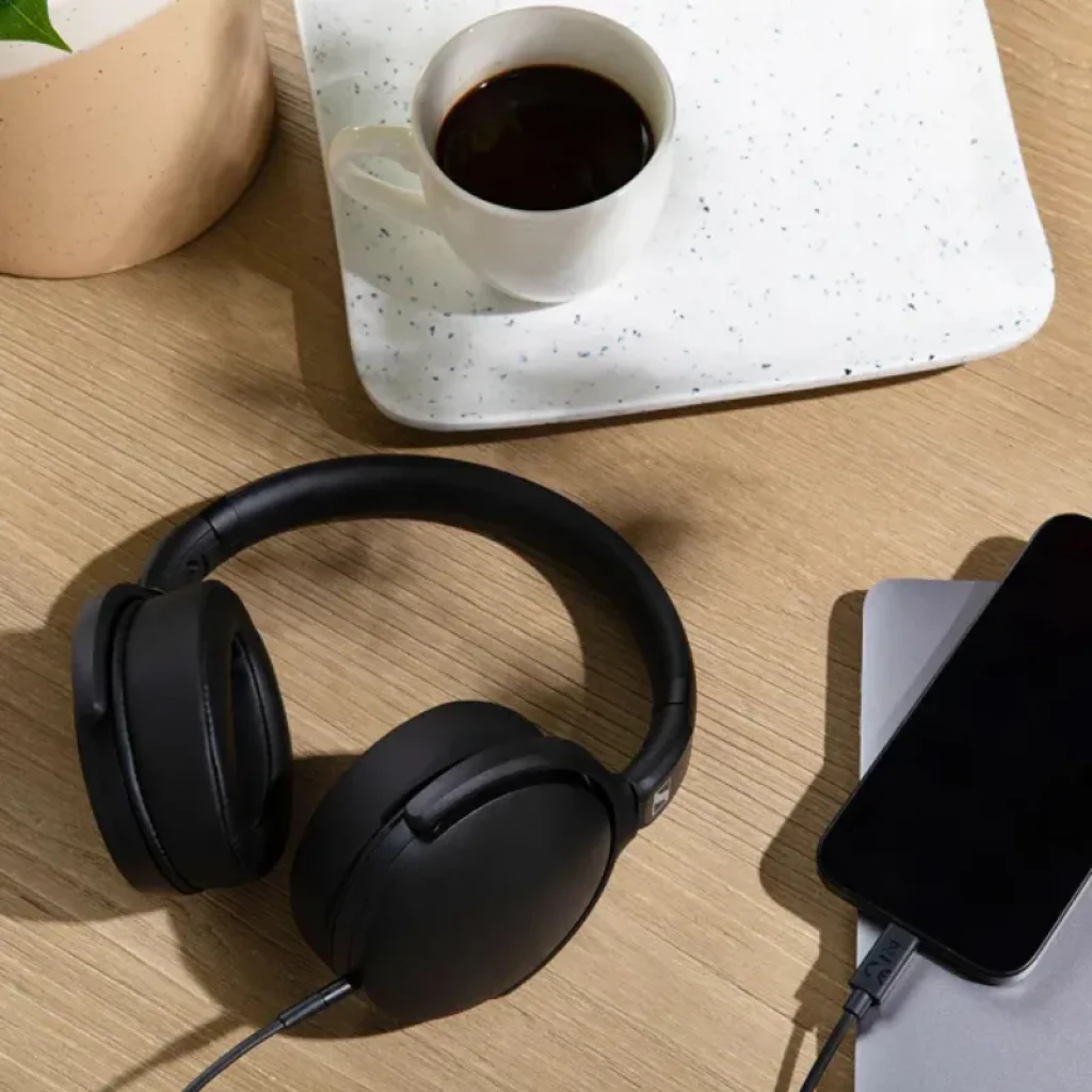 Auriculares Sennheiser HD 400U negros, diseño de diadema cerrada con almohadillas acolchadas y cable USB conectado, junto a taza de café y smartphone sobre