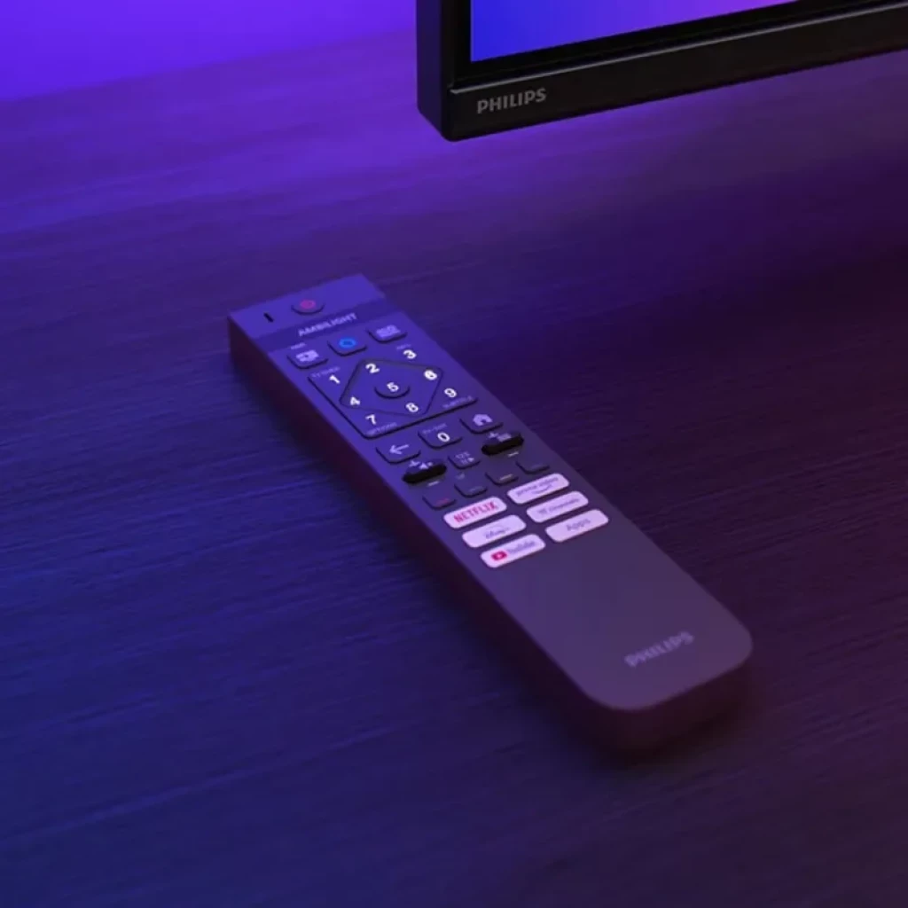 Control remoto Philips con botones iluminados, diseño ergonómico y acceso rápido a apps, junto a borde de TV 55MLED820 con luz ambiental violeta azulada