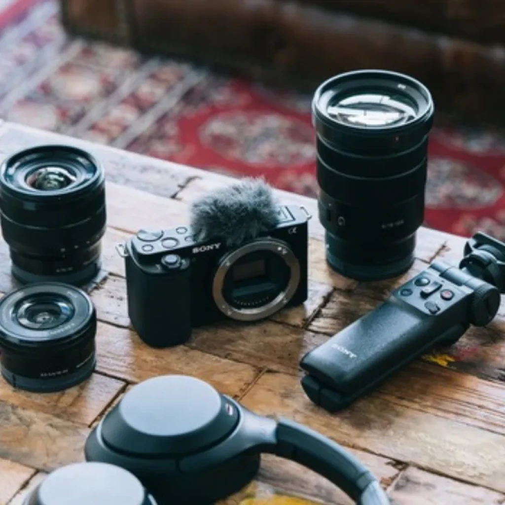 Sony Alpha ZV-E10 cuerpo negro con pantalla articulada, micrófono peludo, empuñadura Bluetooth y tres lentes intercambiables sobre mesa de madera
