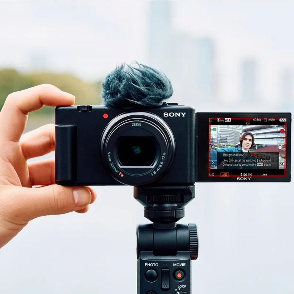 Cámara Sony ZV-1 II para vlogging en 4K, pantalla abatible lateral, micrófono con parabrisas, lente 18-50 mm, montada en empuñadura con controles.