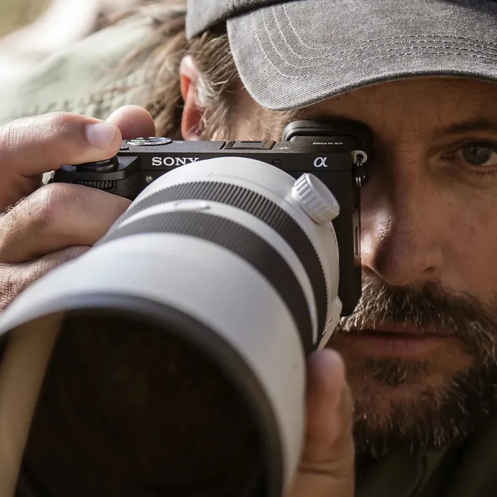 Cámara Sony Alpha 6700 APS-C en uso, cuerpo negro compacto con gran objetivo 18-135mm montado; captura de video 4K 120p, estilo profesional y robusto