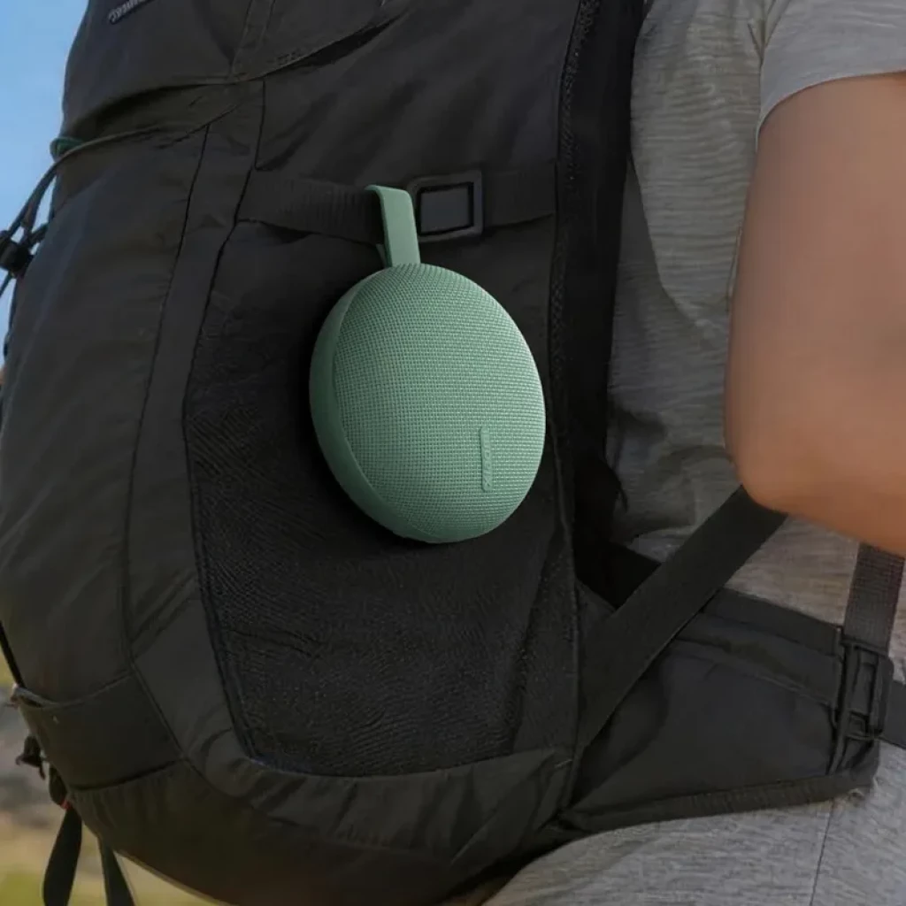 Altavoz portátil compacto color verde menta con correa de silicona, rejilla textil y diseño redondeado, colgado en mochila para uso outdoor IP66