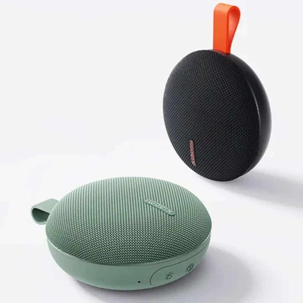 Altavoz portátil redondo negro con malla texturizada, logo Xiaomi naranja y asa superior naranja; controles laterales discretos y diseño compacto IP66