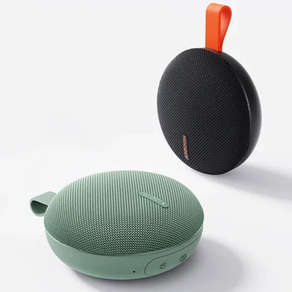 Altavoz portátil redondo negro con malla texturizada, logo Xiaomi naranja y asa superior naranja; controles laterales discretos y diseño compacto IP66