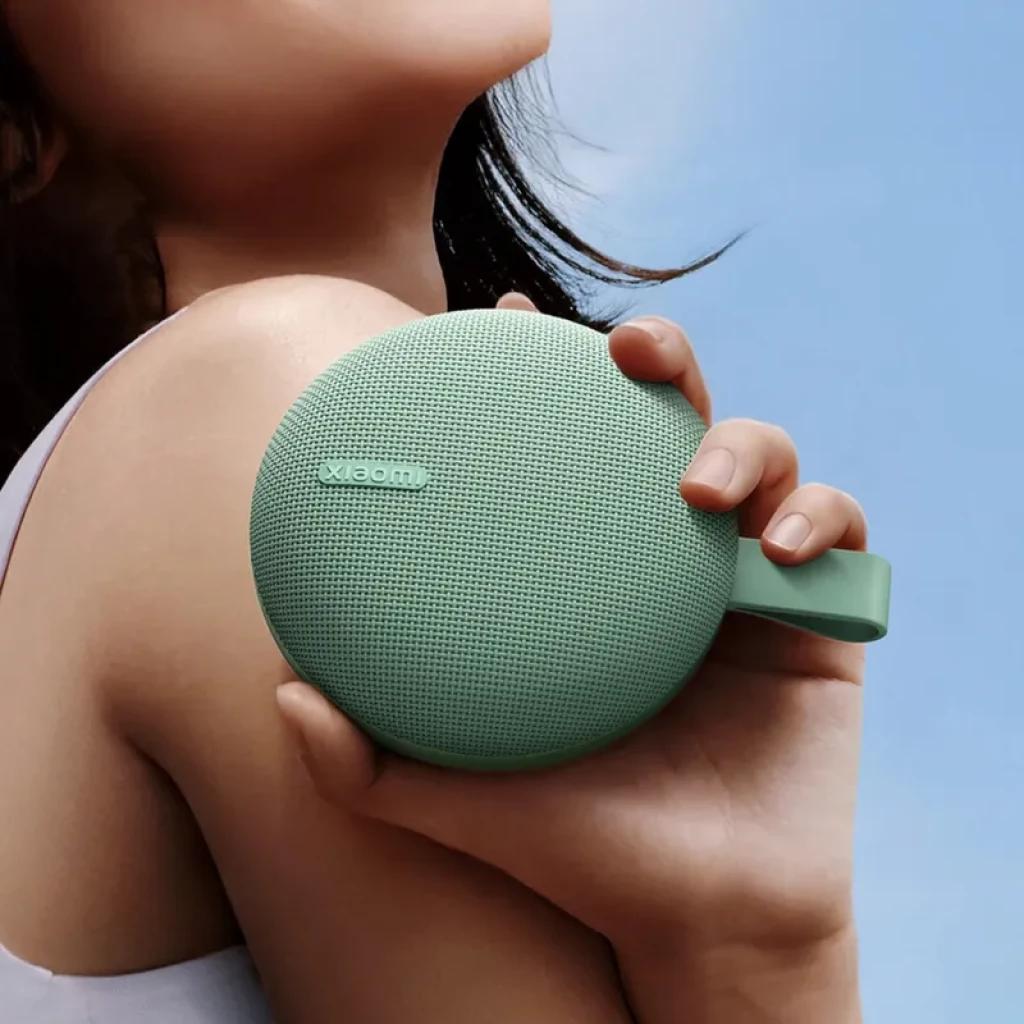 Altavoz portátil redondo Xiaomi verde menta con rejilla texturizada, correa lateral y cuerpo compacto; diseño minimalista resistente para uso diario