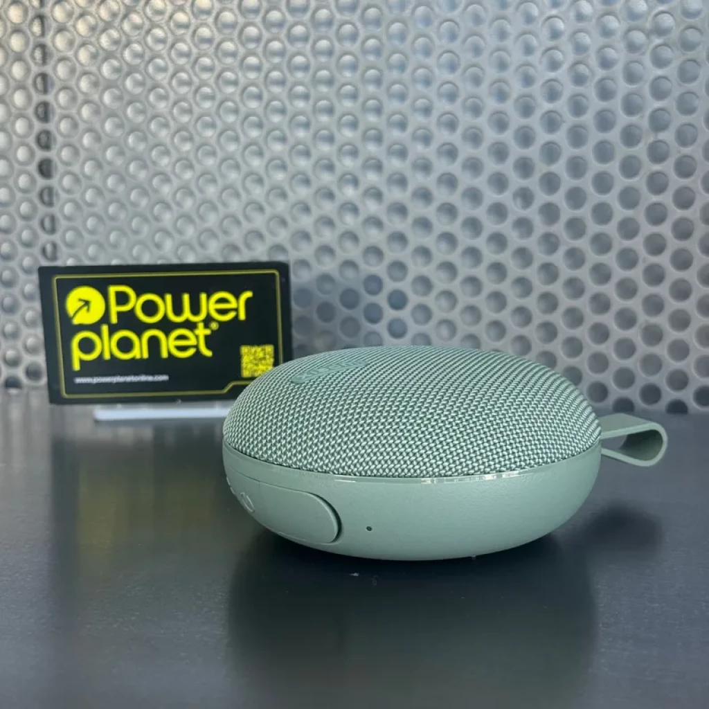 Altavoz portátil verde compacto con rejilla metálica curva, botón lateral y correa corta; diseño redondeado y base plana, acabado mate tono menta