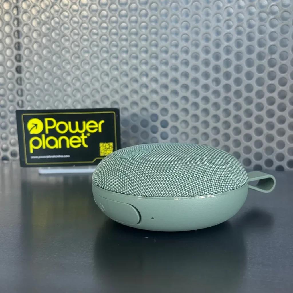 Altavoz portátil verde compacto con rejilla metálica curva, botón lateral y correa corta; diseño redondeado y base plana, acabado mate tono menta