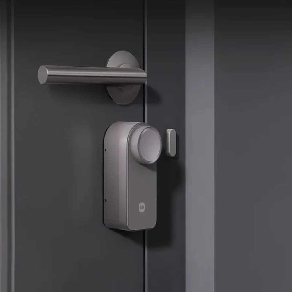 Xiaomi Self-Install Smart Lock sem teclado em acabamento cinza, corpo compacto com botão giratório e sensor lateral, instalado sob a maçaneta na porta.