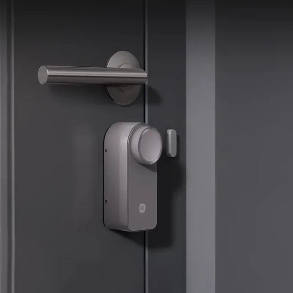 Xiaomi Self-Install Smart Lock sem teclado em acabamento cinza, corpo compacto com botão giratório e sensor lateral, instalado sob a maçaneta na porta.