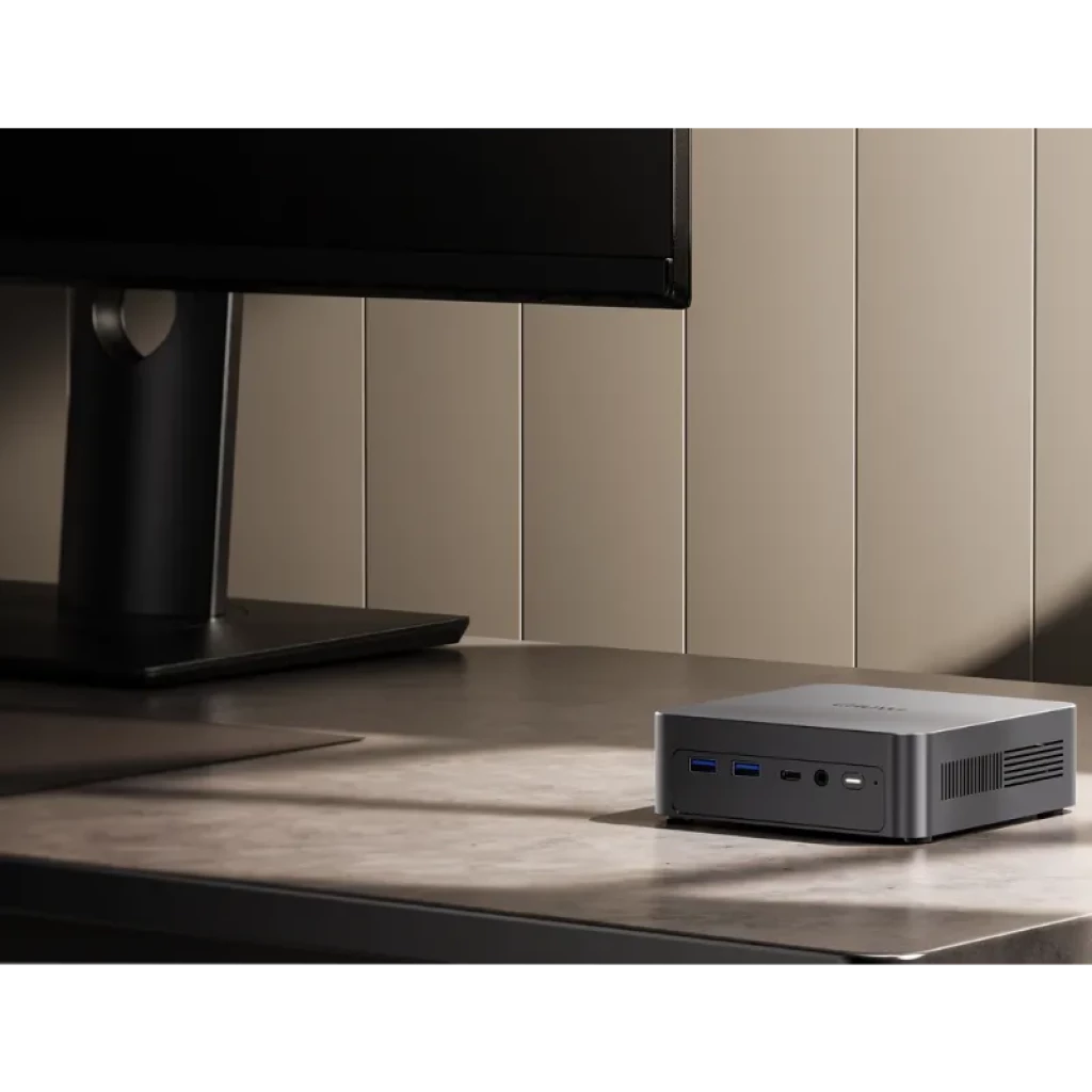 Chuwi AuBox X Mini PC gris compacto en escritorio, frontal con dos USB-A, USB-C, jack y botón de encendido; laterales con rejillas de ventilación