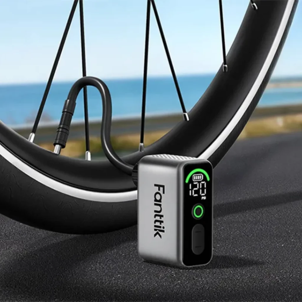 Fanttik X10 Ace Tiny 120 PSI 130g mini inflador eléctrico con pantalla digital, indicador de batería, botón frontal y manguera conectada a rueda de bicicleta