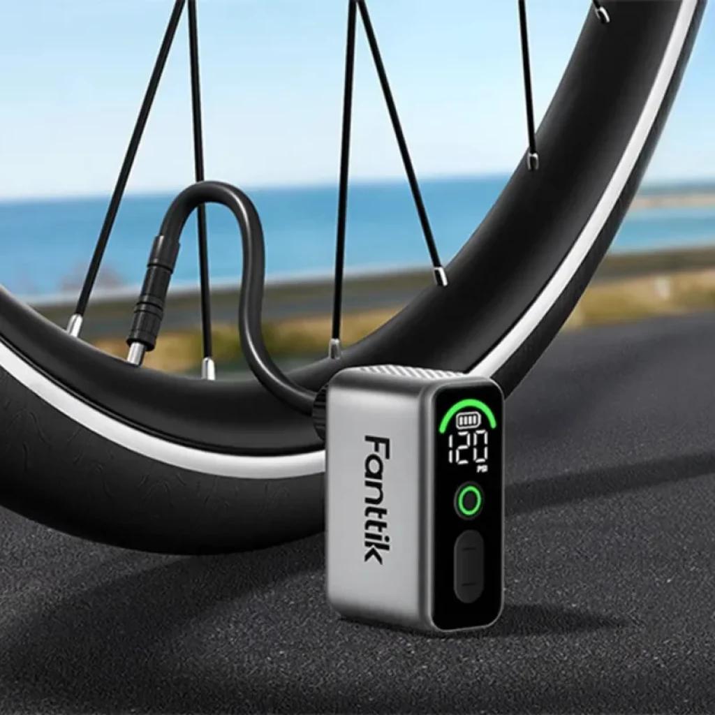 Fanttik X10 Ace Tiny 120 PSI 130g mini inflador eléctrico con pantalla digital, indicador de batería, botón frontal y manguera conectada a rueda de bicicleta