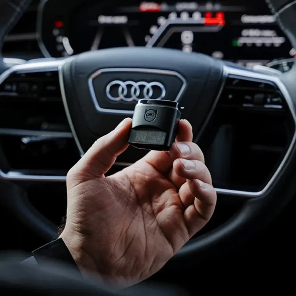 Dispositivo compacto negro con pantalla y logo, conector OBD II portátil en mano, acabado mate; ideal para diagnóstico VAG vía Bluetooth BLE