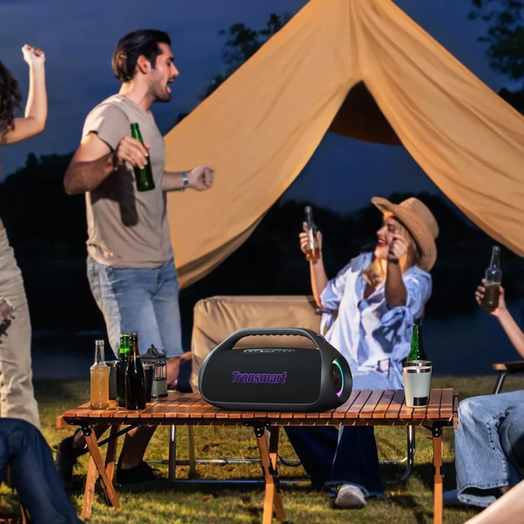 Altavoz Tronsmart Bang 2 negro 90W con asa, rejilla frontal iluminada RGB, forma portátil robusta y botones superiores; ambientado en exterior sobre mesa