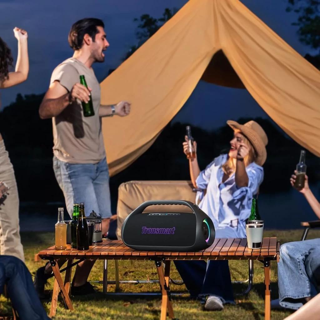 Altavoz Tronsmart Bang 2 negro 90W con asa, rejilla frontal iluminada RGB, forma portátil robusta y botones superiores; ambientado en exterior sobre mesa