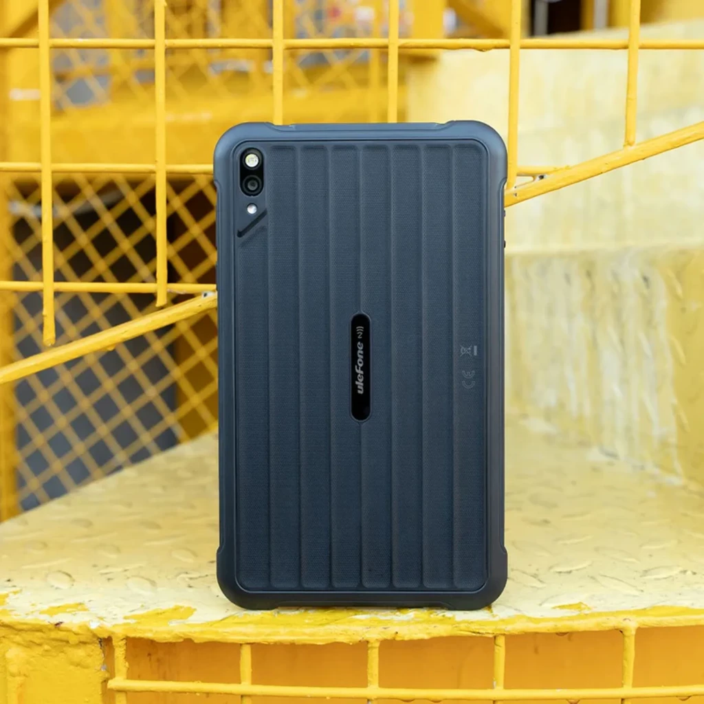 Tableta robusta negra con carcasa acanalada, doble cámara trasera y sellos laterales; diseño resistente ideal para uso industrial y exterior