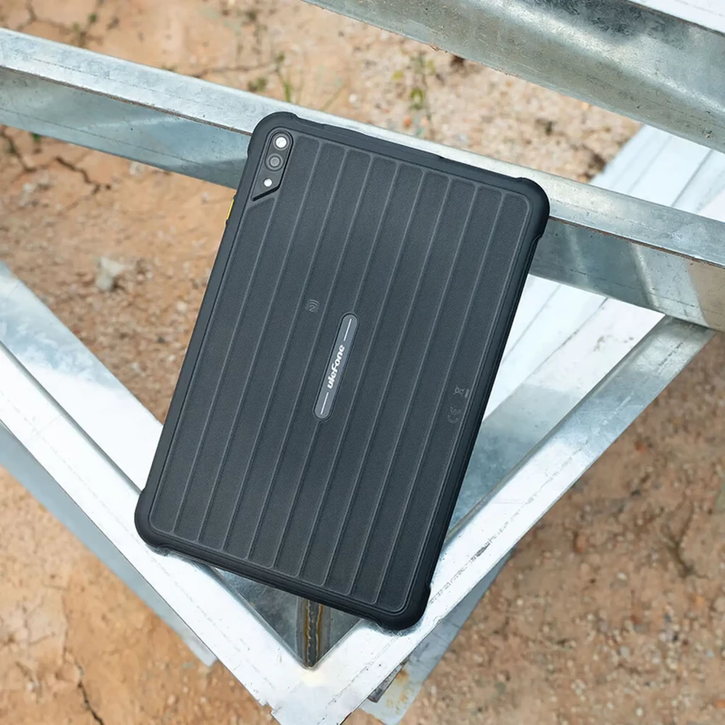 Tablet robusta negra con carcasa acanalada, bordes reforzados y doble cámara trasera vertical con flash; diseño resistente apto para exteriores