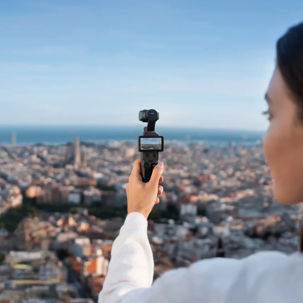 DJI Osmo Pocket 4 Creator Combo 4K 240fps Mic 3 en mano, cámara compacta con gimbal, pantalla integrada y control frontal, capturando ciudad panorámica