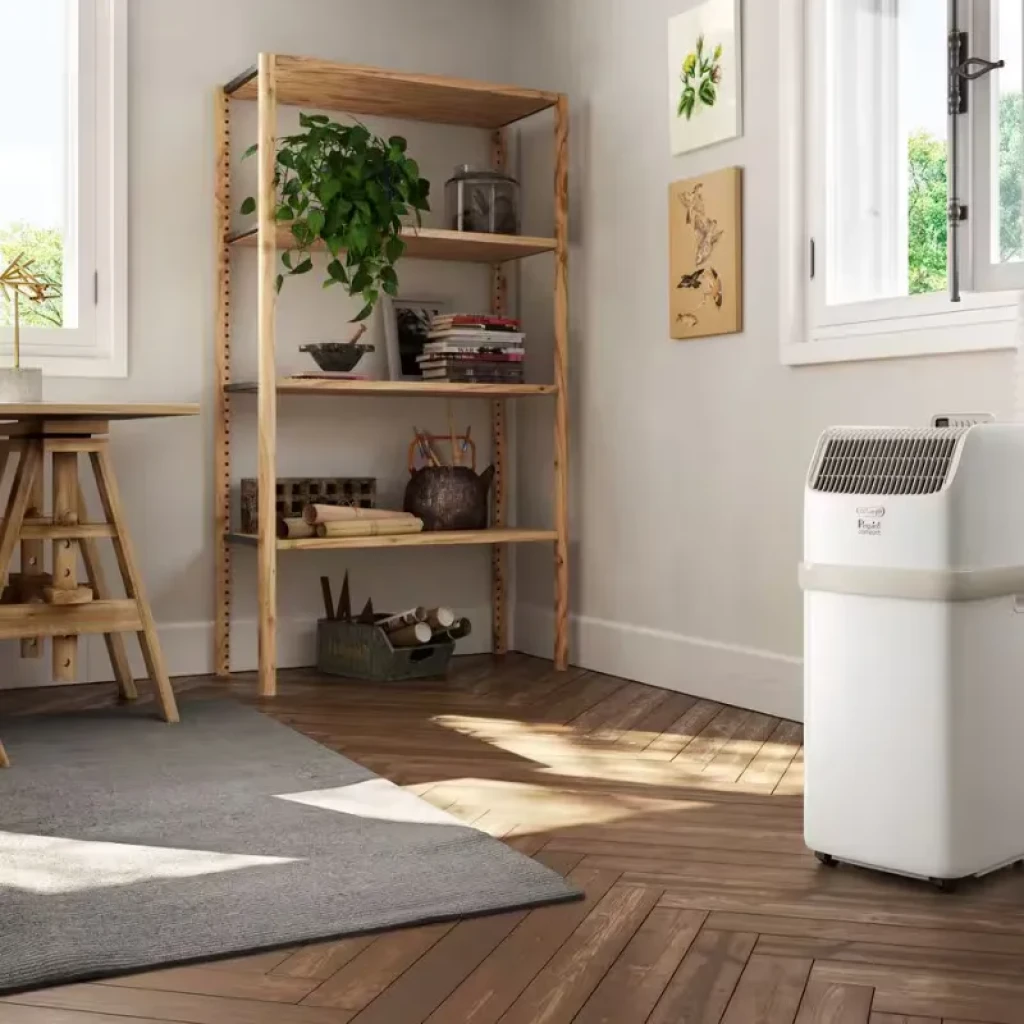 DeLonghi PAC ES72 Classic portátil blanco con rejilla frontal y ruedas, diseño compacto en esquina de sala; panel superior inclinado y salida de aire amplia