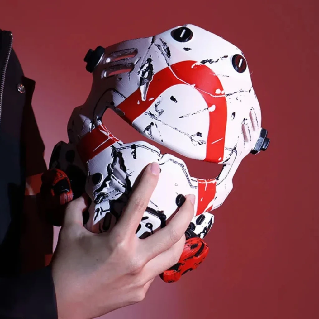 Máscara impresa en 3D estilo futurista en blanco con patrones rojos y detalles negros, tornillos laterales ajustables y acabado texturizado, sostenida con una